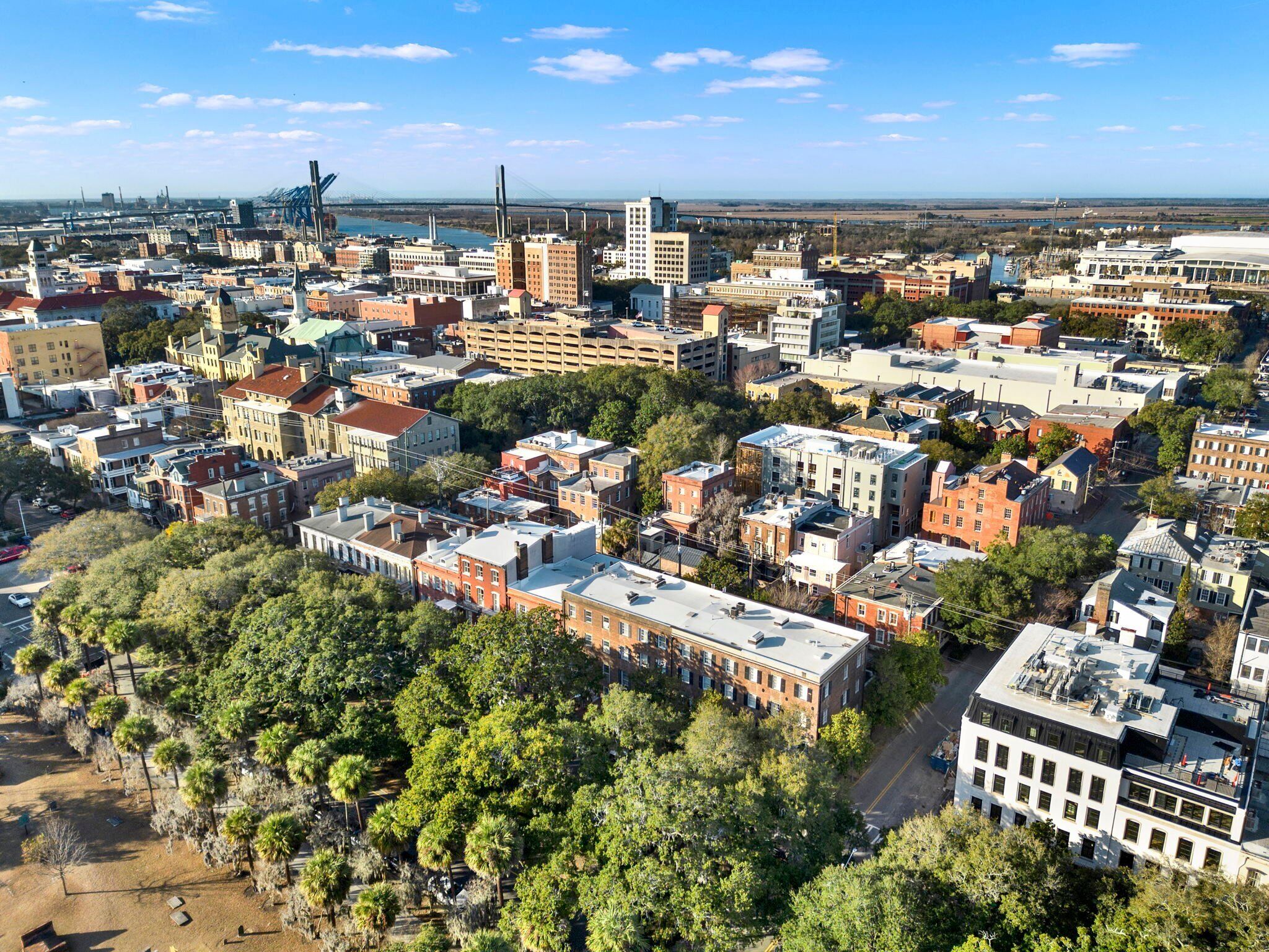An aerial view of a cityscape with various buildings, including a mix of residential and commercial structures, and a prominent bridge in the background.
