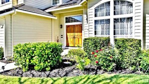 A two-story house with a front porch, a garage, and a well-maintained garden with bushes and flowers. - Grand Executive Luxury Home (Union City)