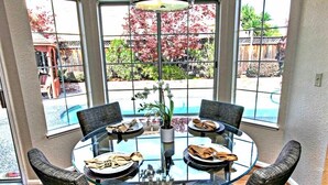 A round glass table with four chairs, a vase with flowers, and plates with napkins. - Grand Executive Luxury Home (Union City)