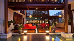 Un espacio interior moderno con suelo de madera, asientos rojos y plantas en macetas.
