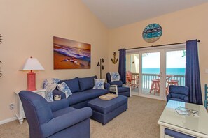 A living room with a sofa, armchairs, a coffee table, and a view of the ocean through a sliding glass door.
