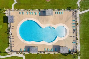 Eine Vogelperspektive auf einen Swimmingpool mit ungewöhnlicher Form, umgeben von Liegestühlen und Sonnenschirmen.