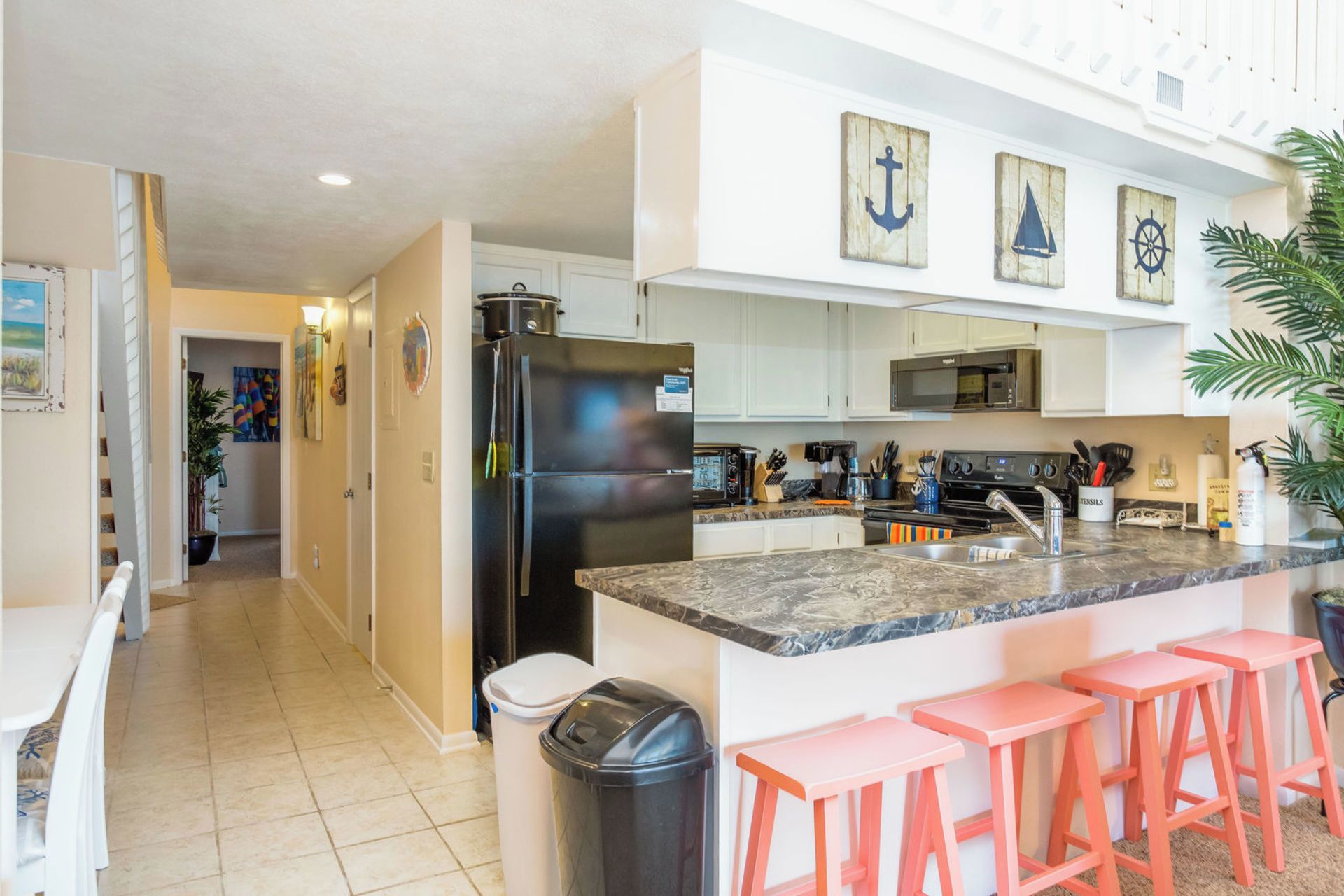 A kitchen with a large island, white cabinets, and a microwave. There are three pink stools at the island.