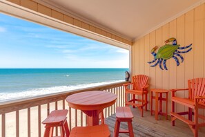A wooden deck with a round table and six chairs, overlooking a beach with a clear view of the ocean. - Top of The Surf - 2BR Oceanfront Surf Condo - Community Pool! Sleeps 8 (Surf City)