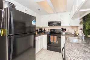A kitchen with white cabinets, a black refrigerator, a microwave, and a stove.