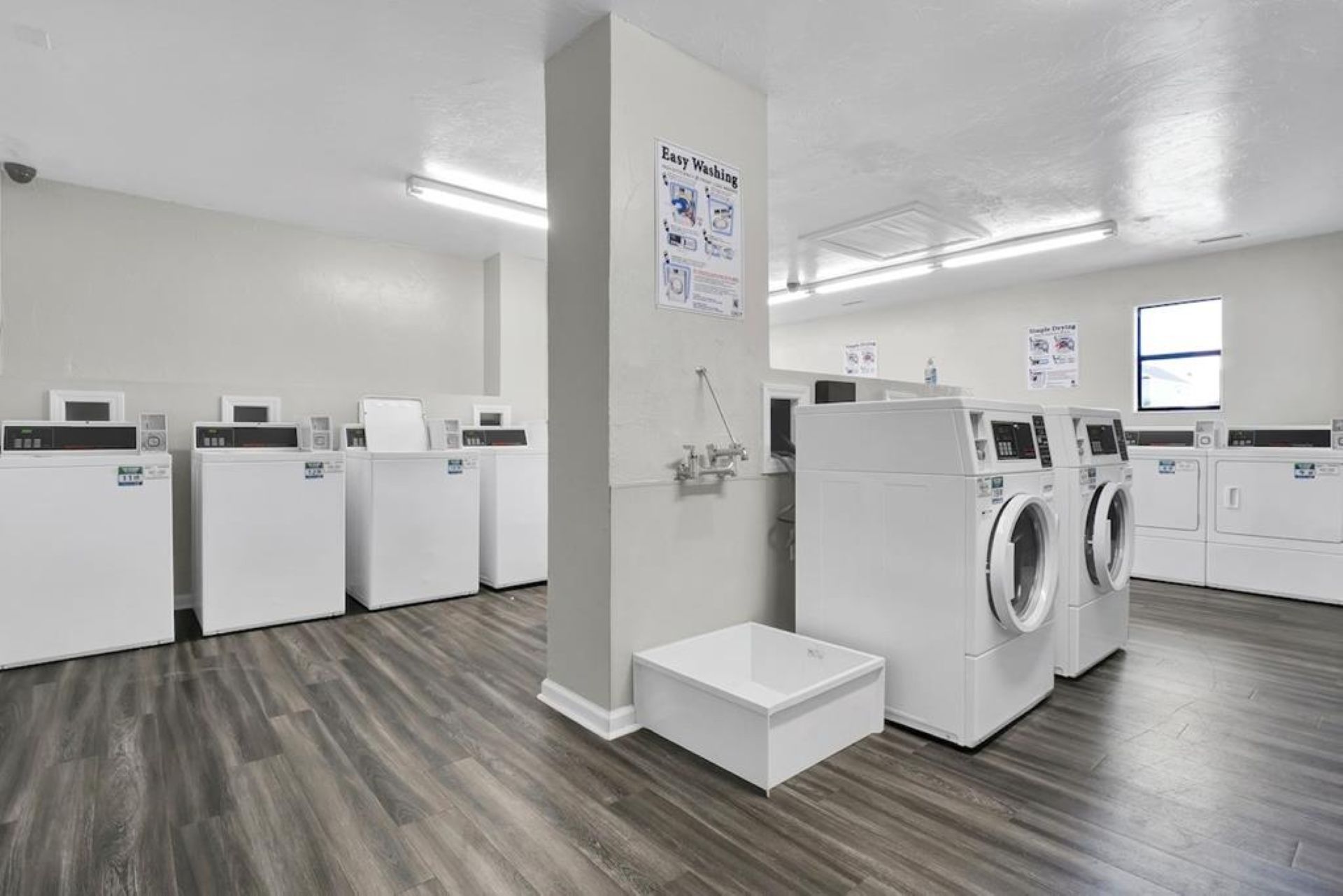 A laundry facility with multiple washing machines and dryers, a small step for accessibility, and instructional posters on the wall.
