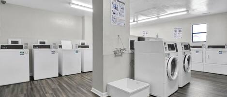 A laundry facility with multiple washing machines and dryers, a small step for accessibility, and instructional posters on the wall.