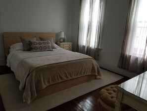 A bedroom with a bed, bedside tables, a nightstand, and a window with curtains.