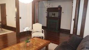 A living room with a wooden floor, a beige armchair, a coffee table with a plant, a fireplace, and a dark-colored sofa.