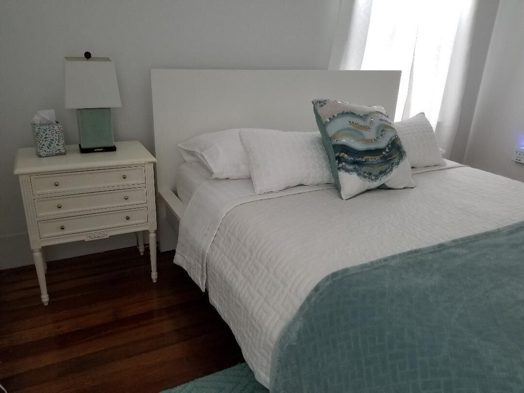 A bedroom with a white bed, a nightstand with a lamp, and a decorative pillow.