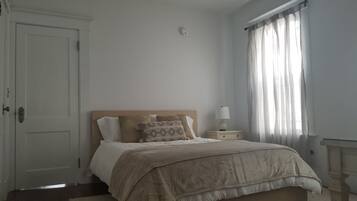 A bedroom with a bed, a nightstand, a lamp, a door, and a window with curtains.