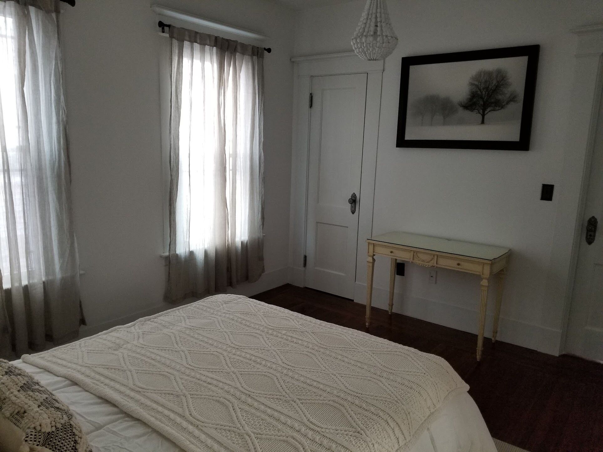 Un dormitorio con cama, mesita de noche, puerta y un cuadro en la pared.