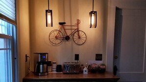 A kitchen area with a wooden countertop, two stools, a hanging bicycle decoration, and a coffee machine.