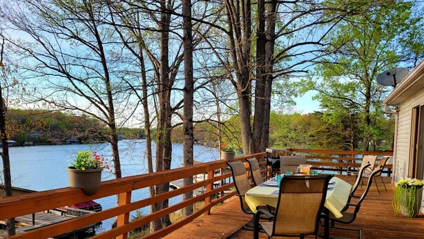 A wooden deck with a table and chairs overlooking a body of water, surrounded by trees. - Gus`s Getaway- Dog friendly home with huge dock with electricity - pool table and old school juke box (Huddleston)