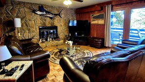 A living room with leather sofas, a stone wall, a fireplace, a TV, and a ceiling fan. - Gus`s Getaway- Dog friendly home with huge dock with electricity - pool table and old school juke box (Huddleston)