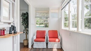 Un couloir étroit avec deux fauteuils en osier dotés de coussins rouges, une plante en pot et une étagère avec des récipients rouges.