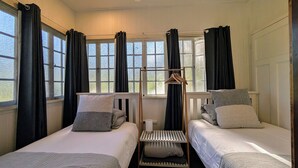 Une chambre avec deux lits, une fenêtre avec des rideaux, un porte-manteau en bois et un radiateur.