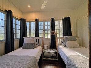 A room with two beds, a window with curtains, a wooden rack with hangers, and a radiator.