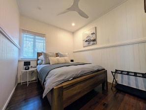 A bedroom with a bed, a desk, a chair, a ceiling fan, and a painting on the wall.