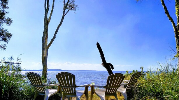 Trois chaises Adirondack sont disposées face à une étendue d’eau, sous un ciel dégagé.