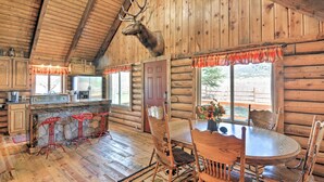 A rustic log cabin interior with a dining table, wooden chairs, a stone fireplace, and a mounted deer head on the ceiling. - Rustic Cabin 20 Mins to Capitol Reef Nat'l Park! (Lyman)