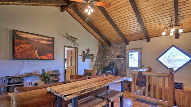 A rustic interior with wooden beams, a stone wall, a large painting, and a wooden bench area. - Rustic Cabin 20 Mins to Capitol Reef Nat'l Park! (Lyman)