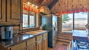 A rustic cabin kitchen with wooden cabinets, a refrigerator, a coffee maker, and a large window overlooking a snowy landscape. - Rustic Cabin 20 Mins to Capitol Reef Nat'l Park! (Lyman)