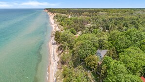 Una propiedad costera con playa, bosque denso y una casa con techo rojo.