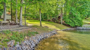 Un cadre paisible au bord d’un lac, avec une terrasse en bois, des chaises et un petit bâtiment.