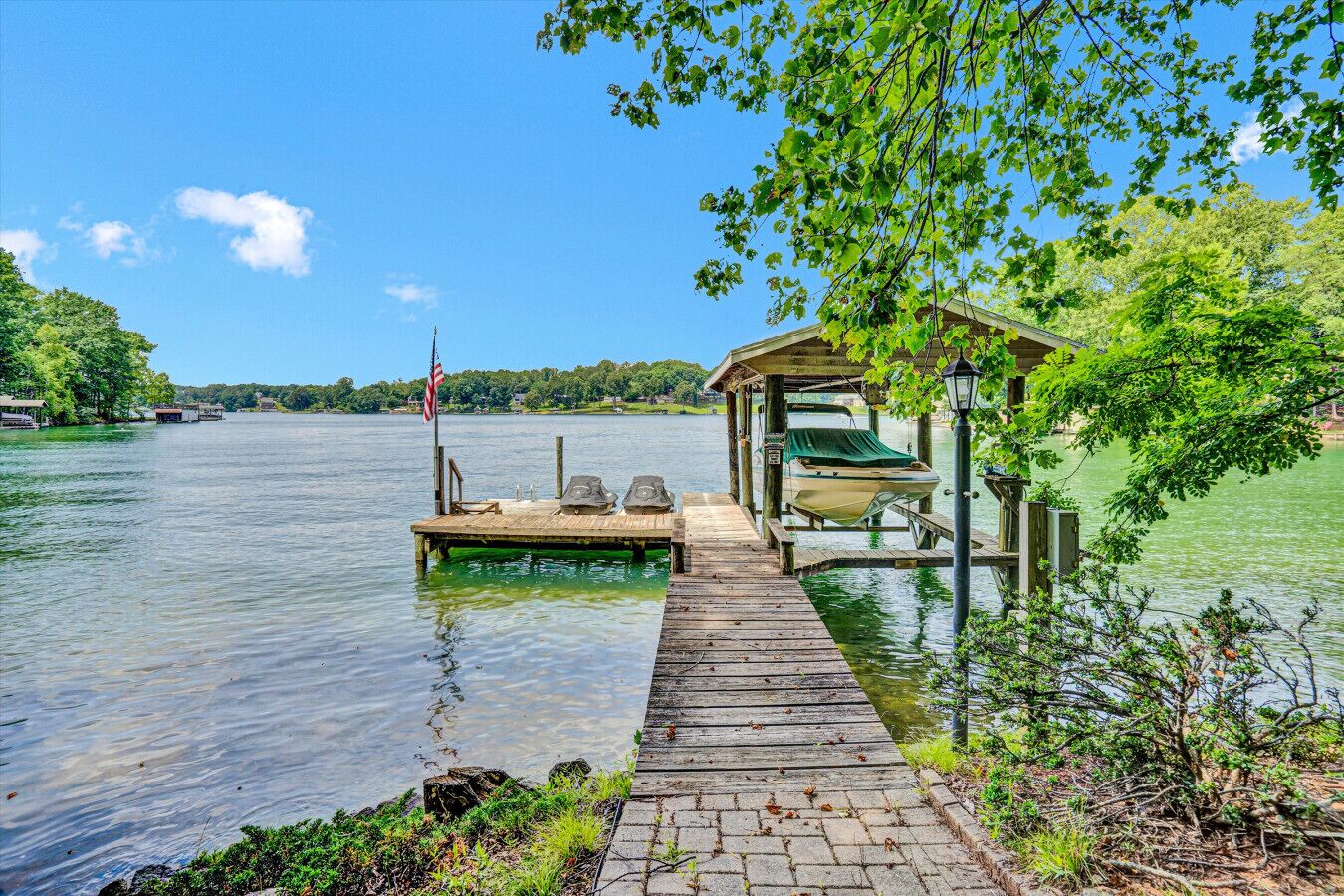 A wooden dock extending into a lake with a covered seating area and a boat docked on the pier.