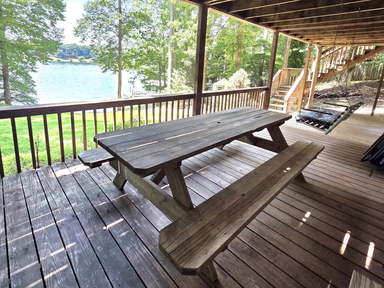 A wooden deck with a picnic table and benches, overlooking a lake.