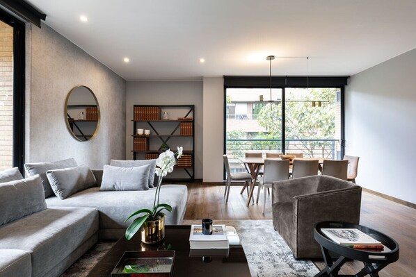 A modern living room with a grey sofa, a coffee table, and a dining area with chairs and a table. - ATTIK STUNNING SUPERIOR  301 (Bogotá)
