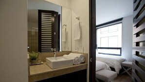A modern bathroom with a large mirror, a sink, and a towel rack. There is a window providing natural light and a view of the outside. - ATTIK STUNNING SUPERIOR  301 (Bogotá)