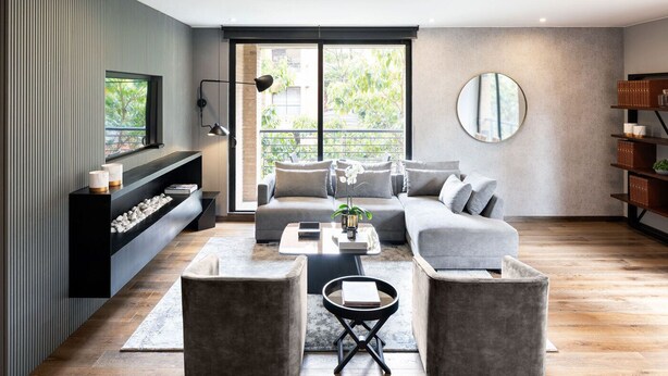A modern living room with a sectional sofa, two armchairs, a coffee table, and a fireplace. There is a large window with a view of greenery outside. - ATTIK STUNNING SUPERIOR  301 (Bogotá)