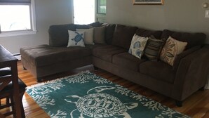 A living room with a brown sectional sofa, a teal patterned rug, and a framed landscape painting on the wall. - Beach Cottage with Outdoor Patio & Grill, 8 min. Walk to Beach (Old Orchard Beach)