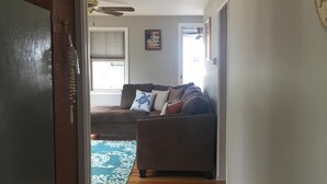A living room with a brown sofa, a blue rug, and a wooden floor. - Beach Cottage with Outdoor Patio & Grill, 8 min. Walk to Beach (Old Orchard Beach)