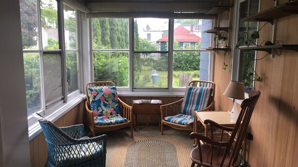 A cozy room with large windows, wicker chairs, a small table, and a lamp. - Beach Cottage with Outdoor Patio & Grill, 8 min. Walk to Beach (Old Orchard Beach)