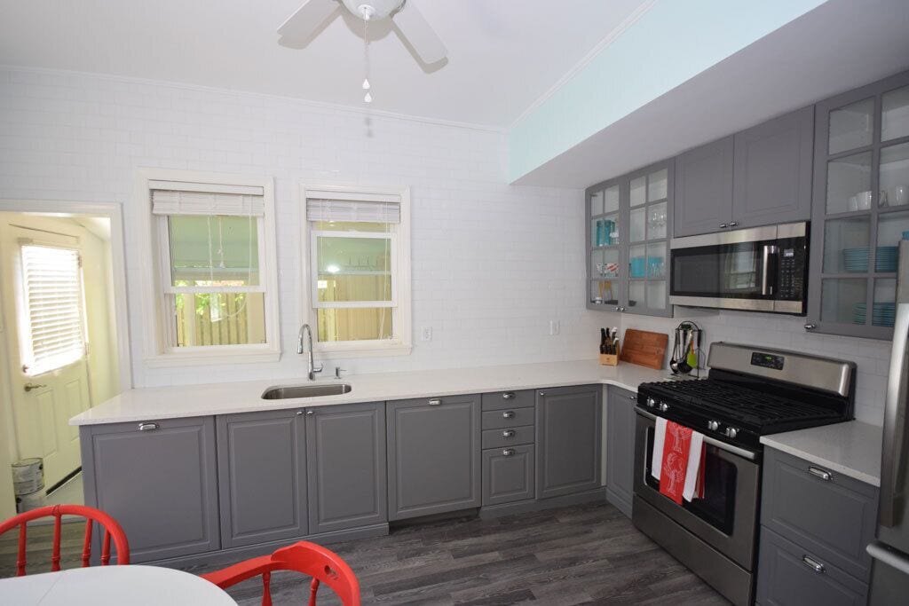 A kitchen with grey cabinets, a stainless steel stove, a microwave, and a window with blinds.