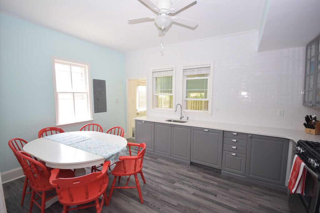 A kitchen with grey cabinets, a white countertop, and a red dining table with chairs.