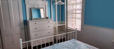 Une chambre à coucher comprenant un lit, une commode, un miroir et une fenêtre avec des stores.