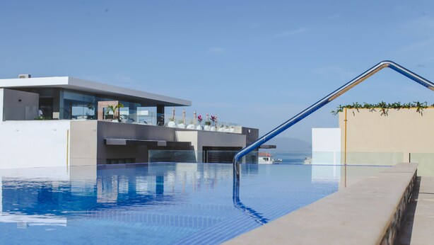 A modern pool with clear blue water, a metal ladder, and a view of the ocean. - Extraordinary condo in Urban complex! 2BD Condo for rent in Old Town, Puerto val (Puerto Vallarta)