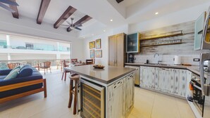 A modern kitchen with a central island, wooden cabinets, and a dining area with a sofa and chairs. - Extraordinary condo in Urban complex! 2BD Condo for rent in Old Town, Puerto val (Puerto Vallarta)