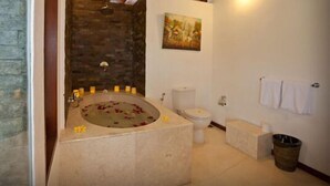A bathroom with a stone sink, a bathtub with rose petals, a toilet, and a trash can.