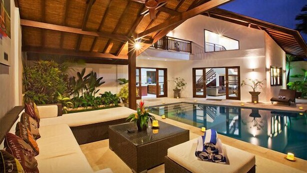 A luxurious indoor pool area with a high ceiling, comfortable seating, and a large window overlooking the pool.