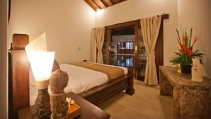 A bedroom with a bed, a nightstand, a lamp, a window with curtains, and a view of the outside.