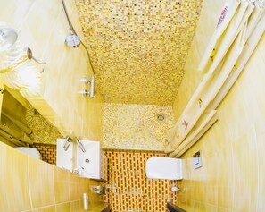 Une salle de bain avec un mur recouvert de mosaïques jaunes, une baignoire blanche et un espace douche.
