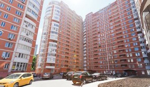 Un immeuble résidentiel de grande hauteur, doté de nombreux balcons et d’un espace de stationnement à l’avant.