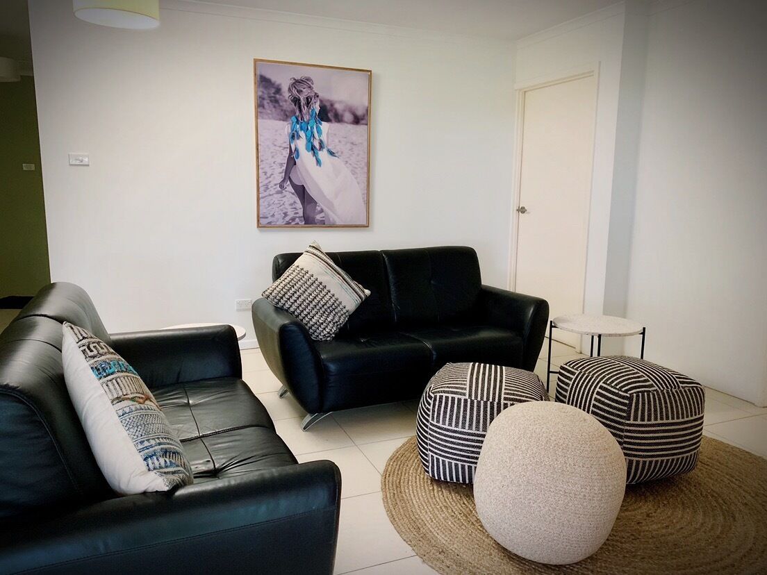 Ein modernes Wohnzimmer mit einem schwarzen Ledersofa, einem runden Hocker und einem kleinen Tisch.