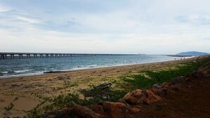 Une plage avec une jetée qui s’avance dans l’eau, un terrain rocheux et une végétation clairsemée.