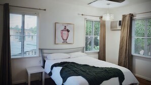 Une chambre à coucher avec un lit, un ventilateur de plafond, une fenêtre avec des stores et un tableau au mur.
